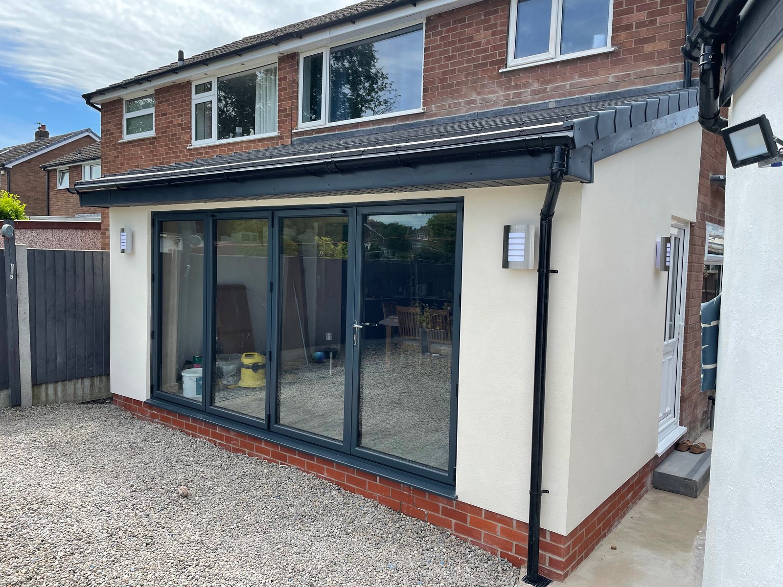 Cream rendered rear extension with anthracite sliding doors on a red-brick house