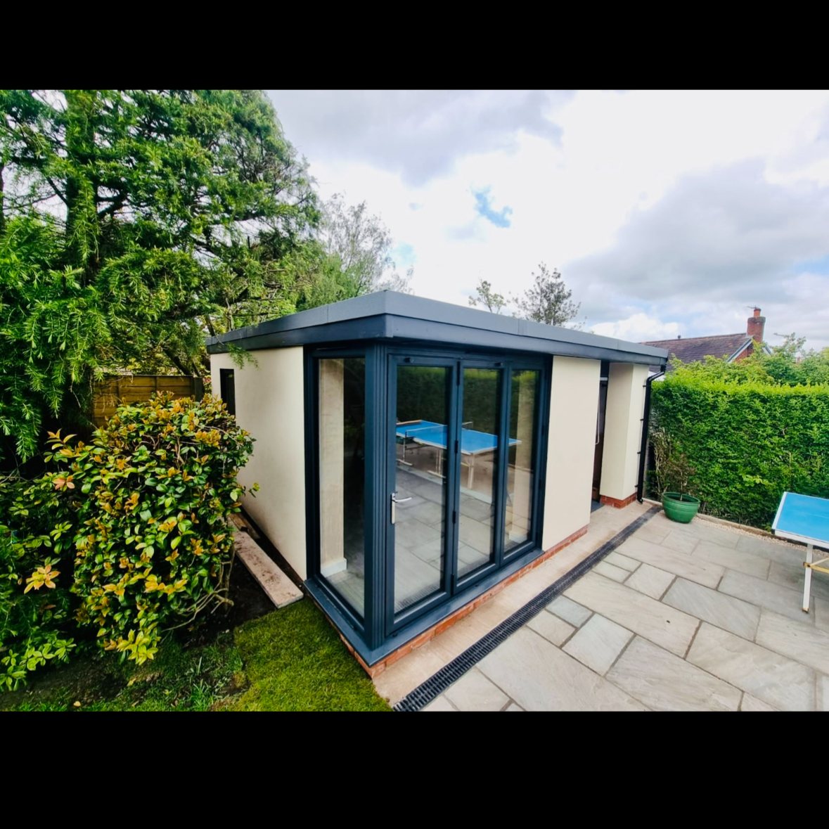 Rendered garden room with anthracite bifold doors and grey stone patio