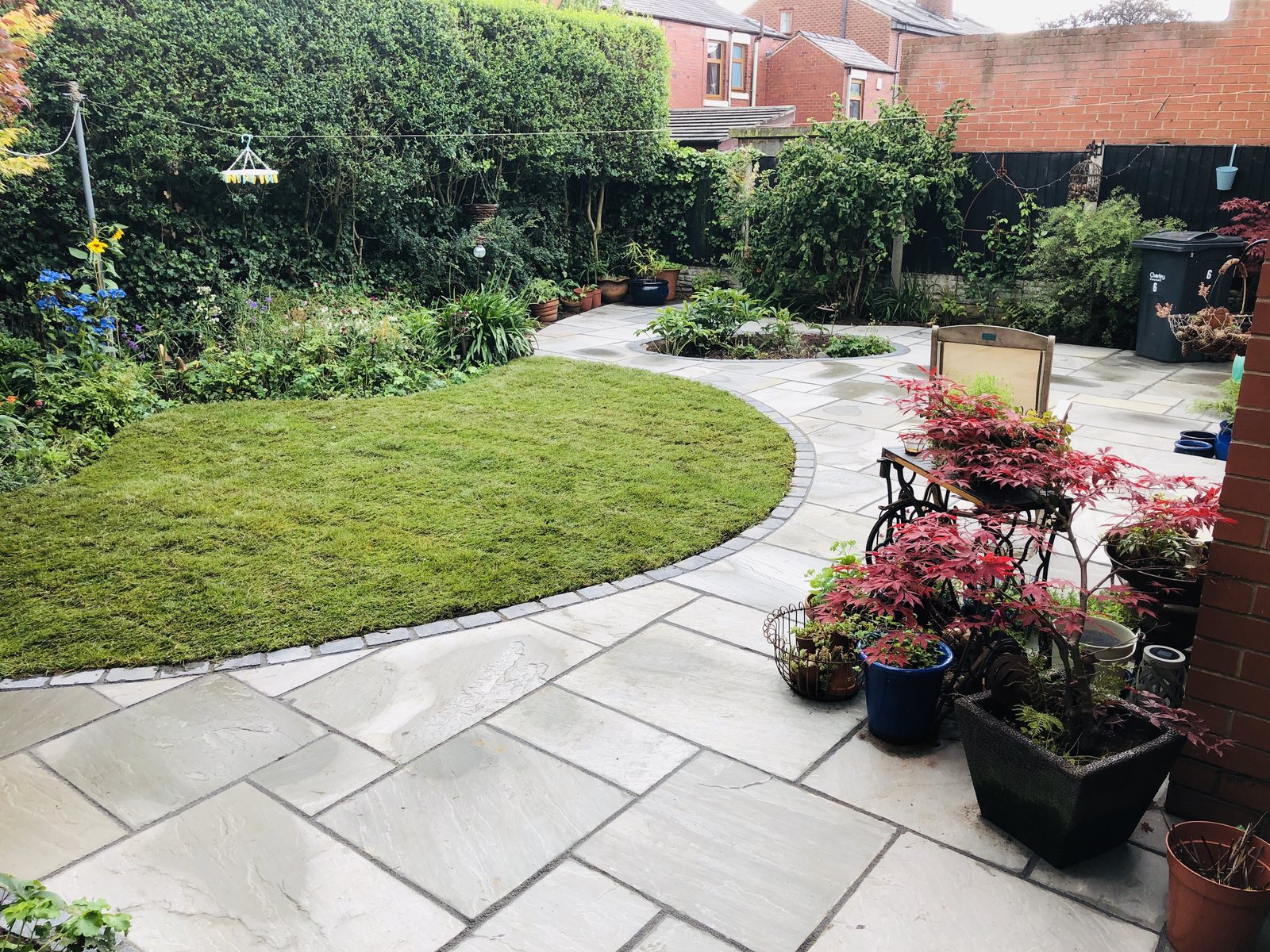 Grey flagstone patio with charcoal sett border around a curved lawn