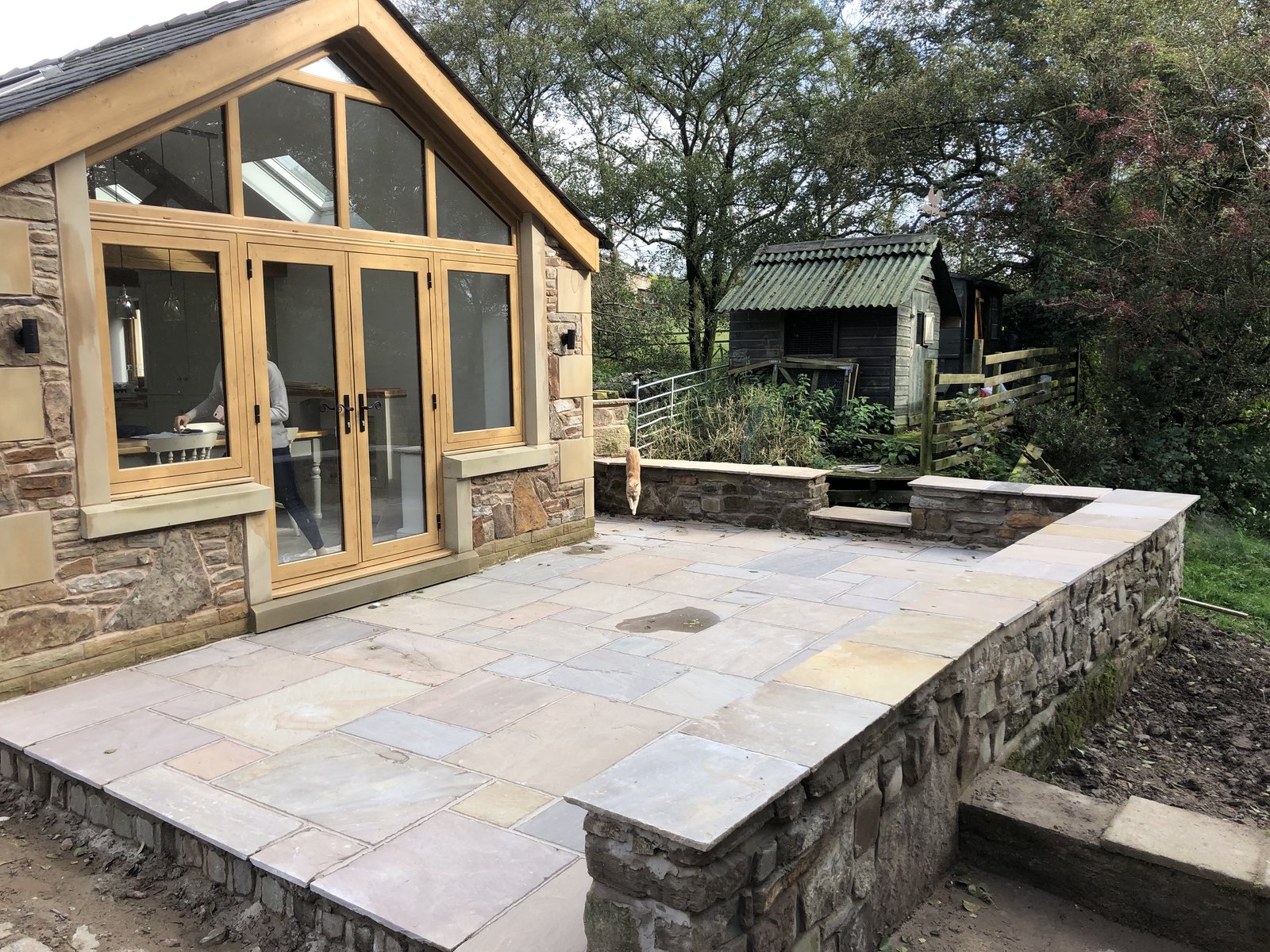 Stone-built extension with oak-framed glass gable opening onto Indian sandstone patio