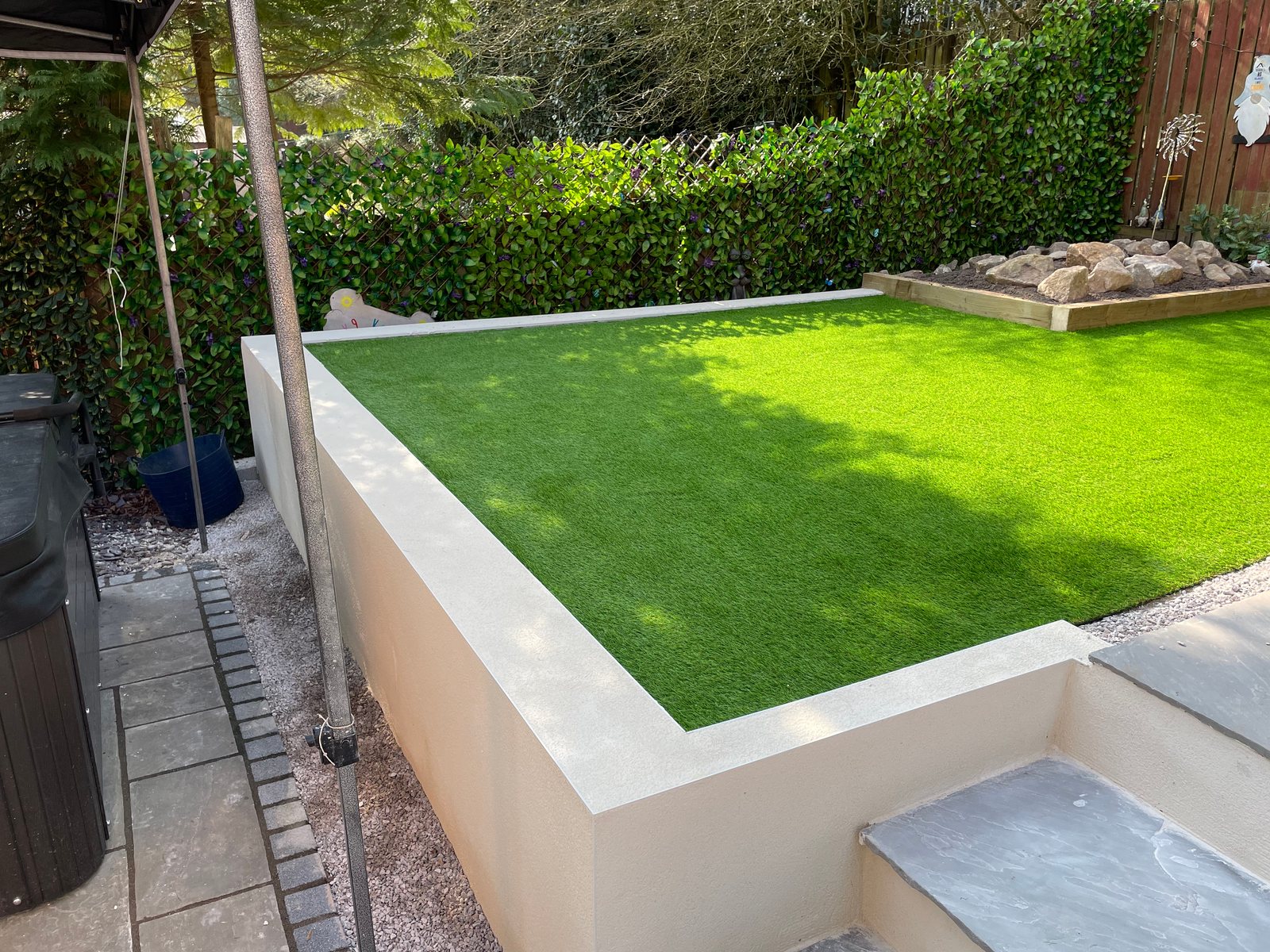 Raised artificial lawn with rendered retaining wall, slate steps and stone patio
